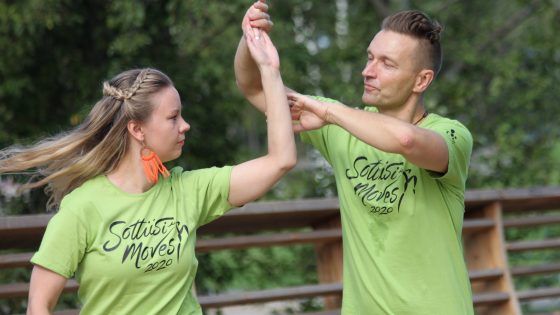 Pari tanssii ulkona SottiisiMovesin vihreissä t-paidoissa. Taustalla näkyy vehreitä puita.