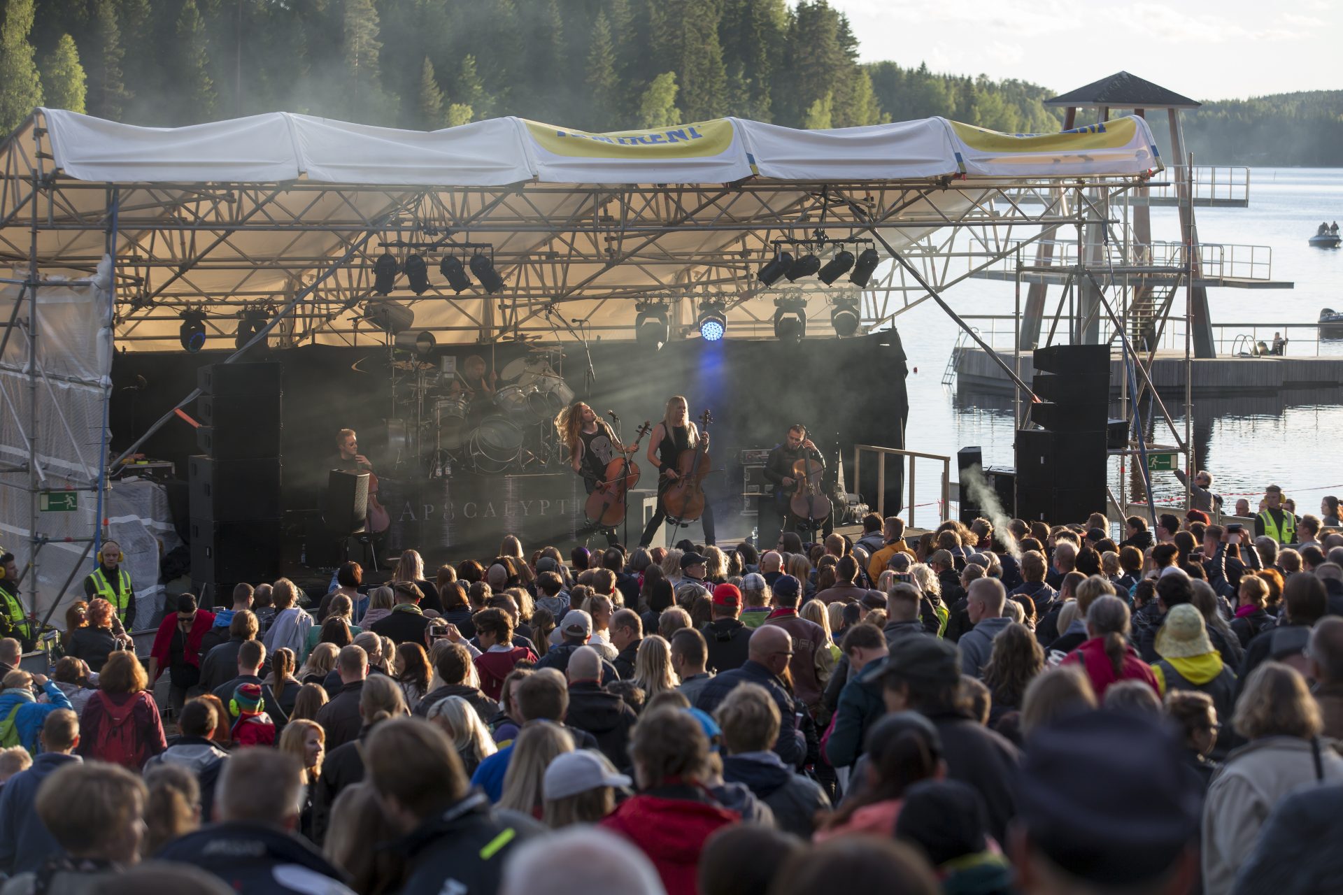 Selloilla metallimusiikkia soittava Apocalyptica-yhtye esiintyy suurelle yleisölle järven rannassa kesäiltana.