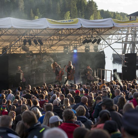 Selloilla metallimusiikkia soittava Apocalyptica-yhtye esiintyy suurelle yleisölle järven rannassa kesäiltana.